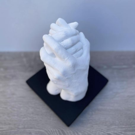 Empreinte moulage Famille Sculture de mains entrelacées en plâtre blanc sur une base noire.
